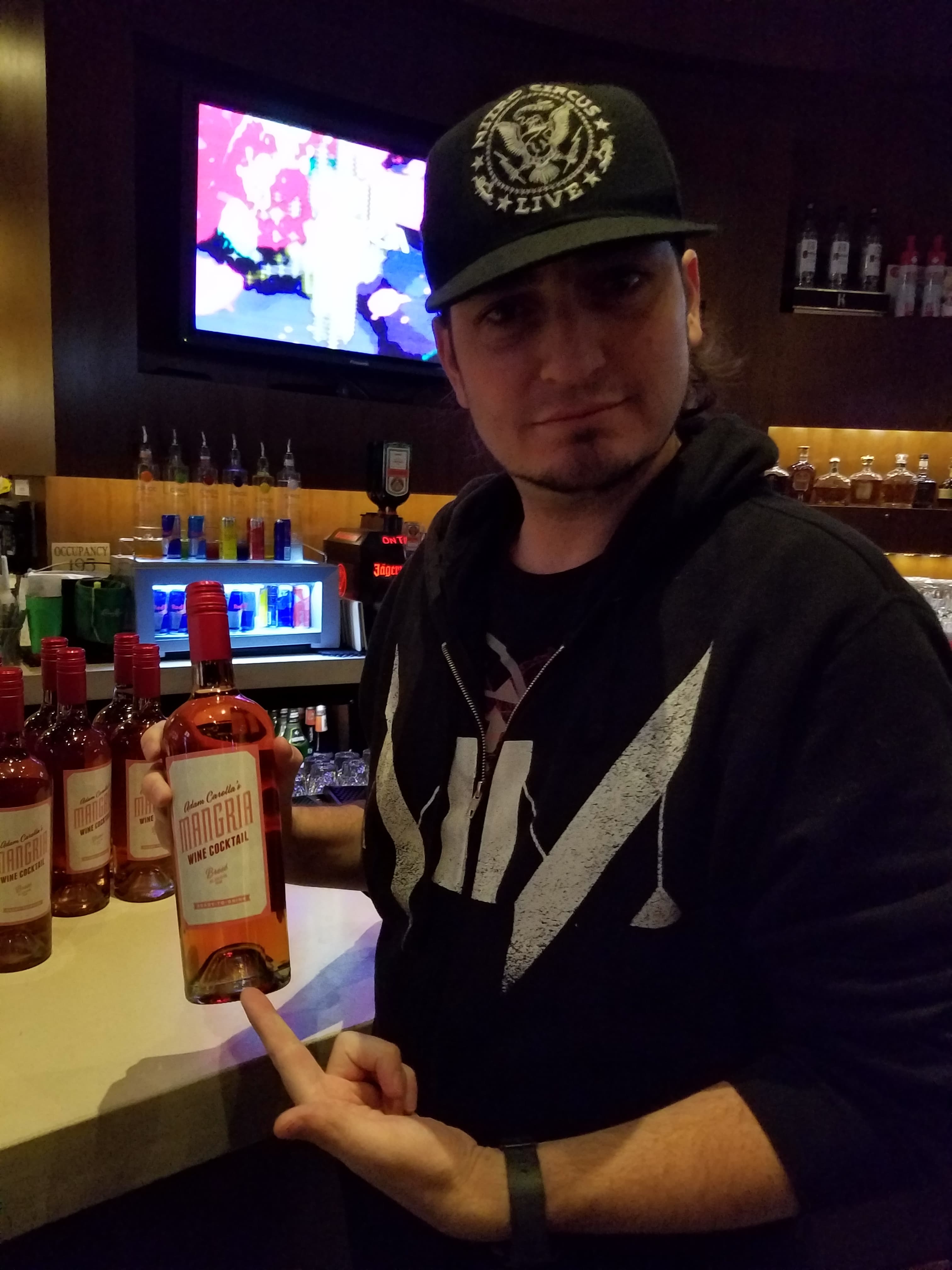 Kronik at Aura Night Club for the Adam Carolla Mangria release, pointing at bottles behind the bar