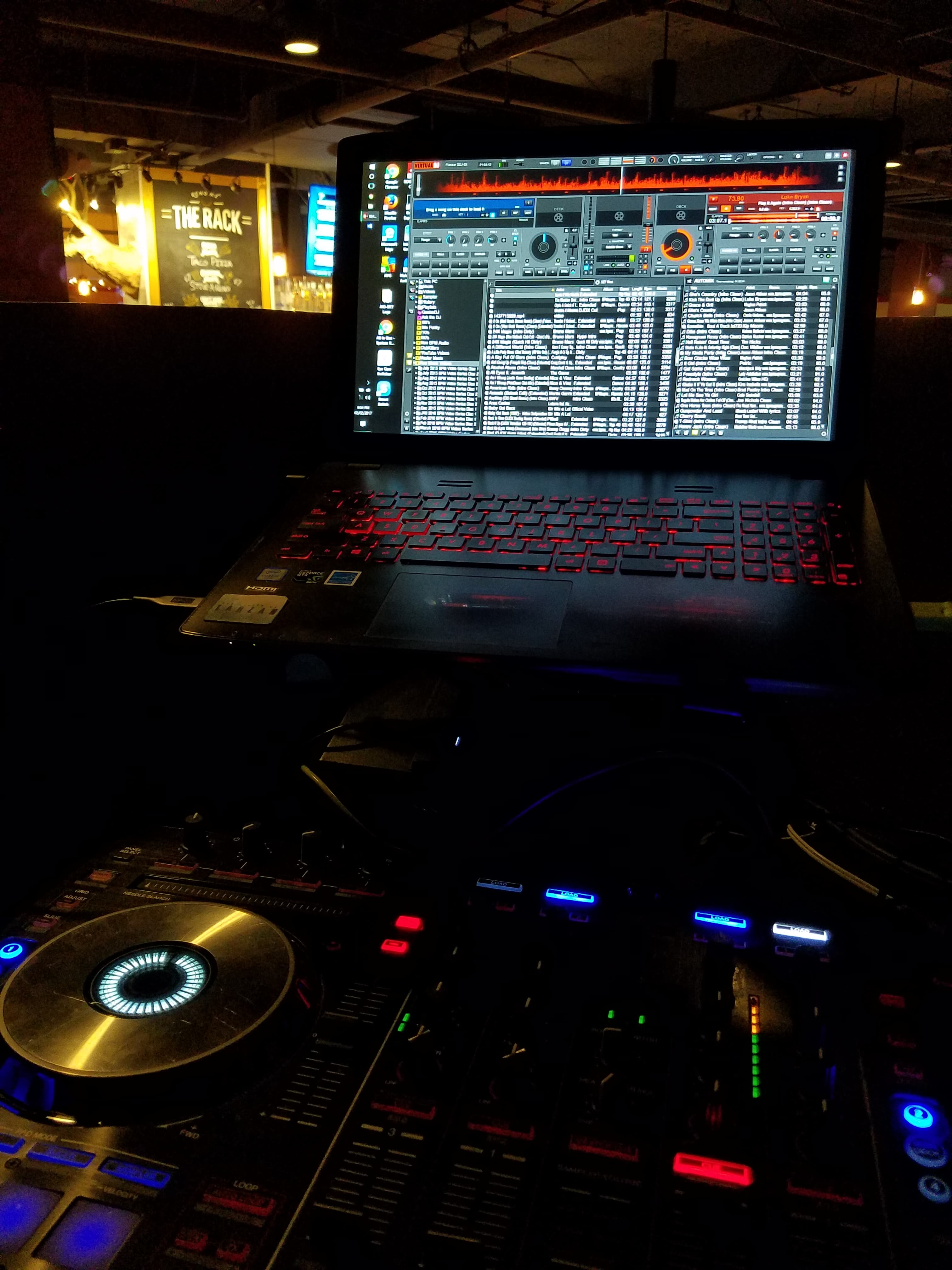 Serato DJ laptop and Pioneer controller in the booth with The Rack sign in the background