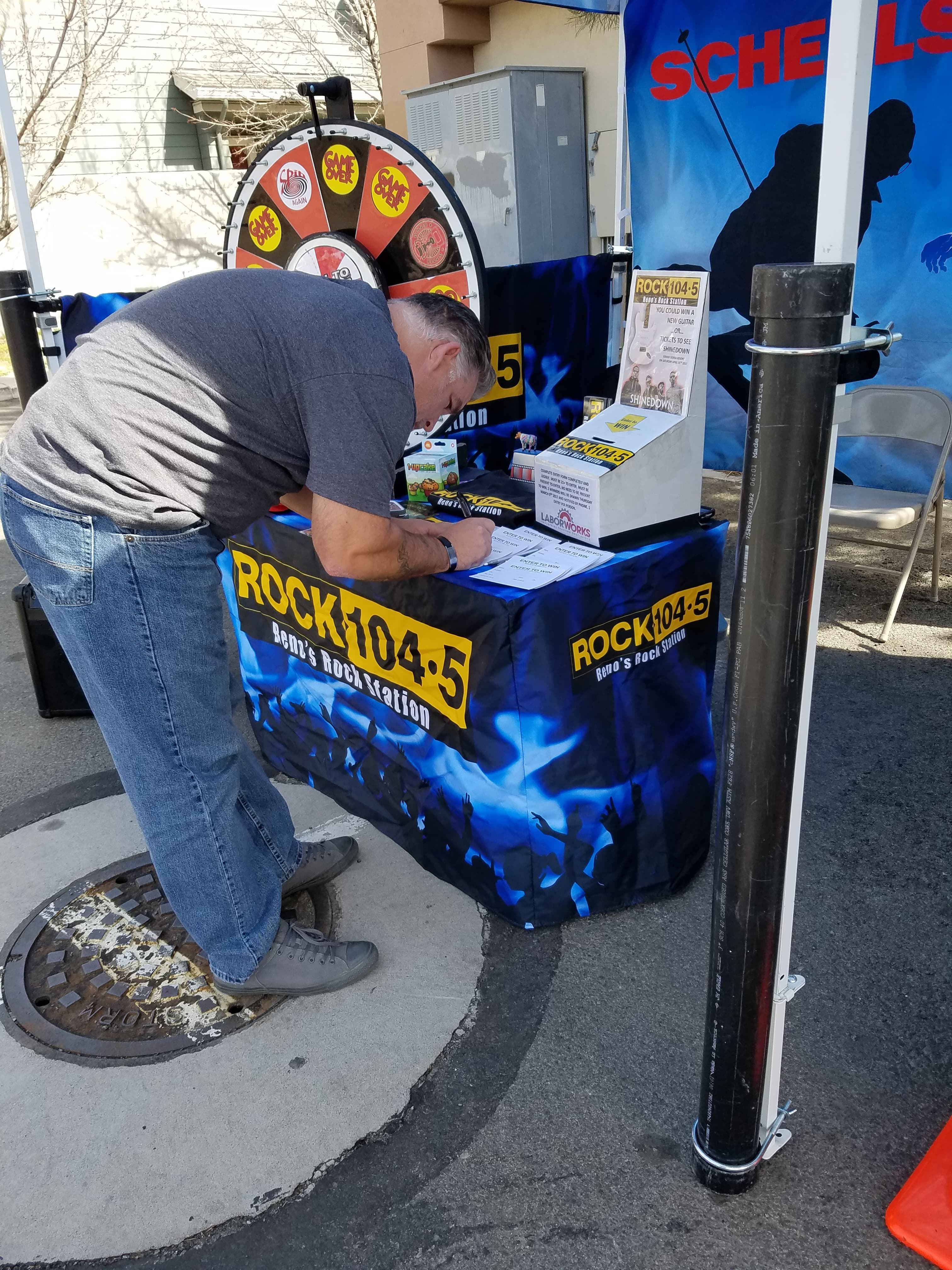Staff member writing at the ROCK 104.5 KDOT prize-wheel table during a Scheels activation