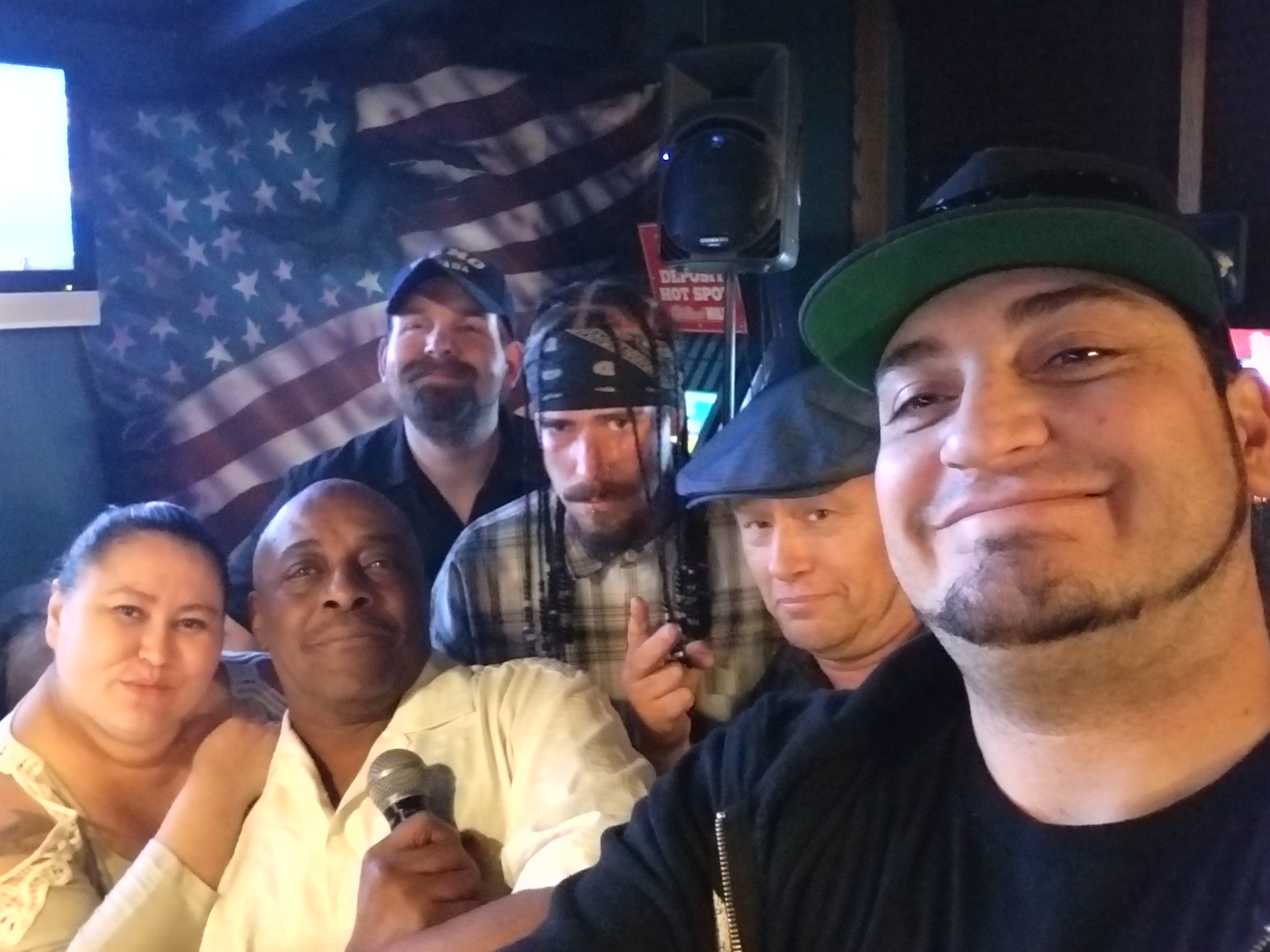 Kronik group selfie with performers and guests in a club with speakers and stage flags