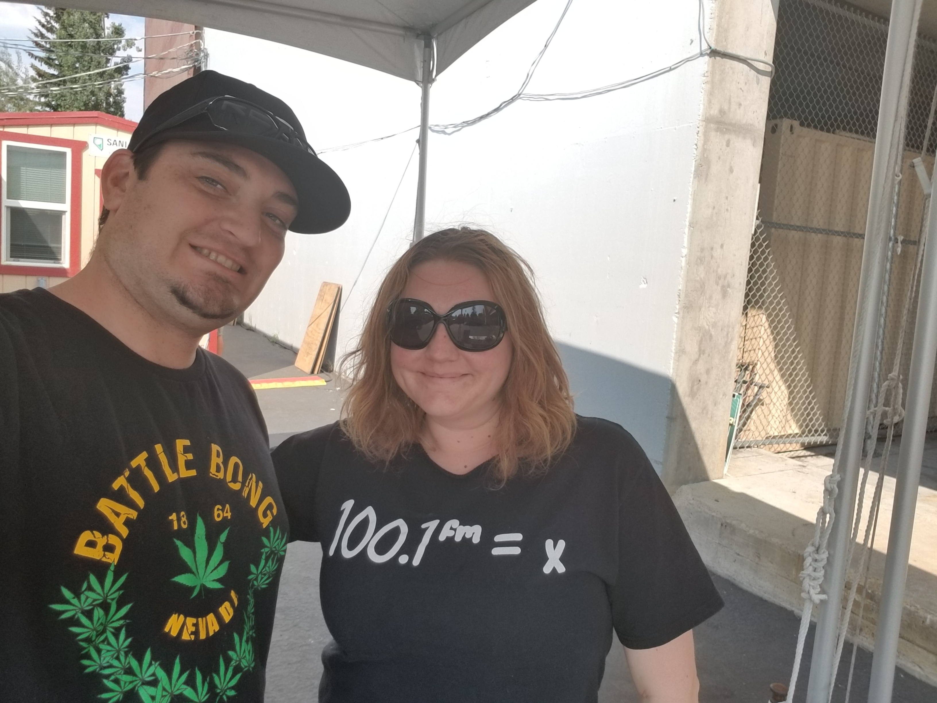 Kronik outdoors with a colleague in a 100.1 FM radio station shirt under a tent