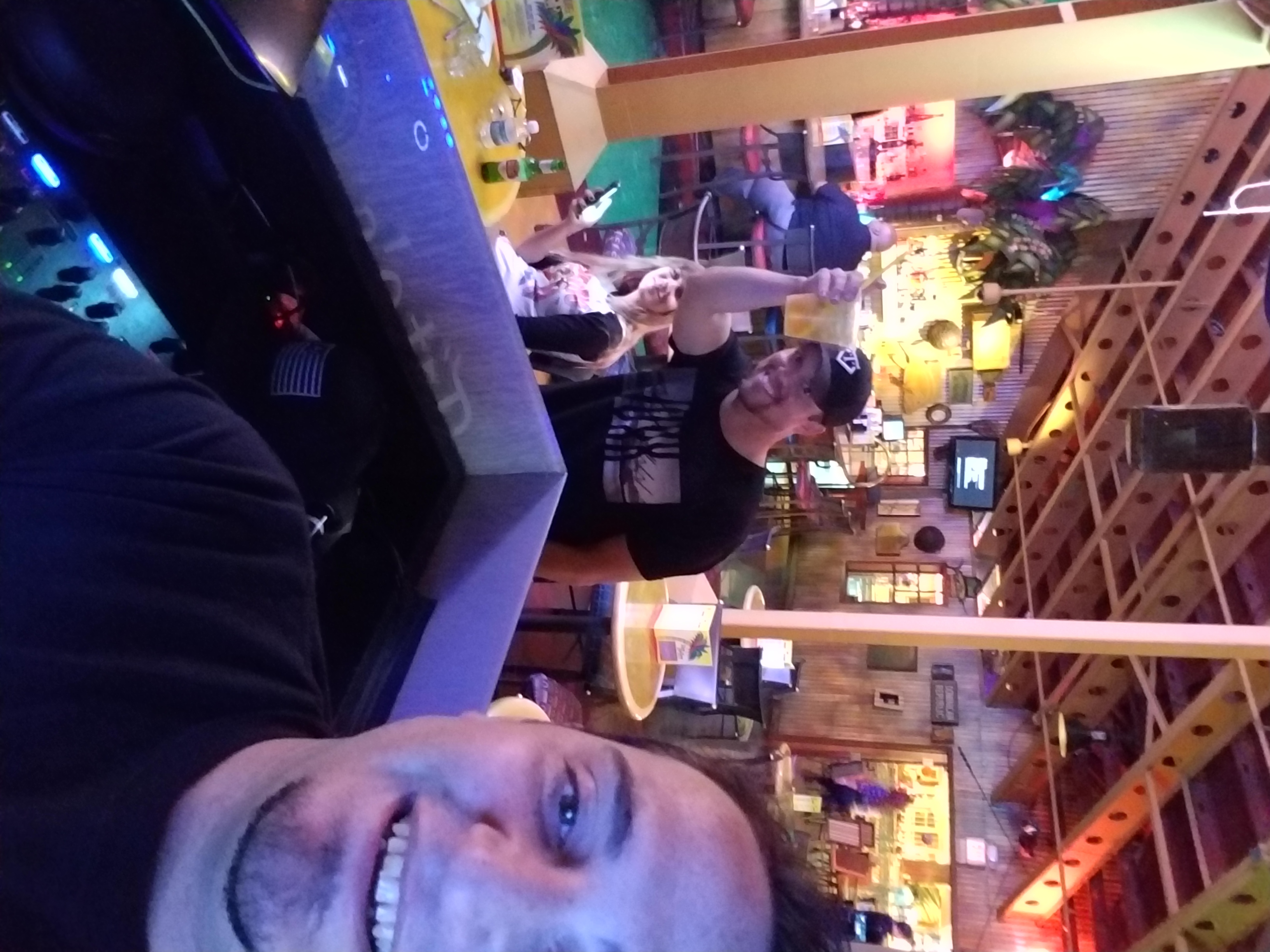 Kronik selfie from the DJ booth with guests and a packed bar room behind him