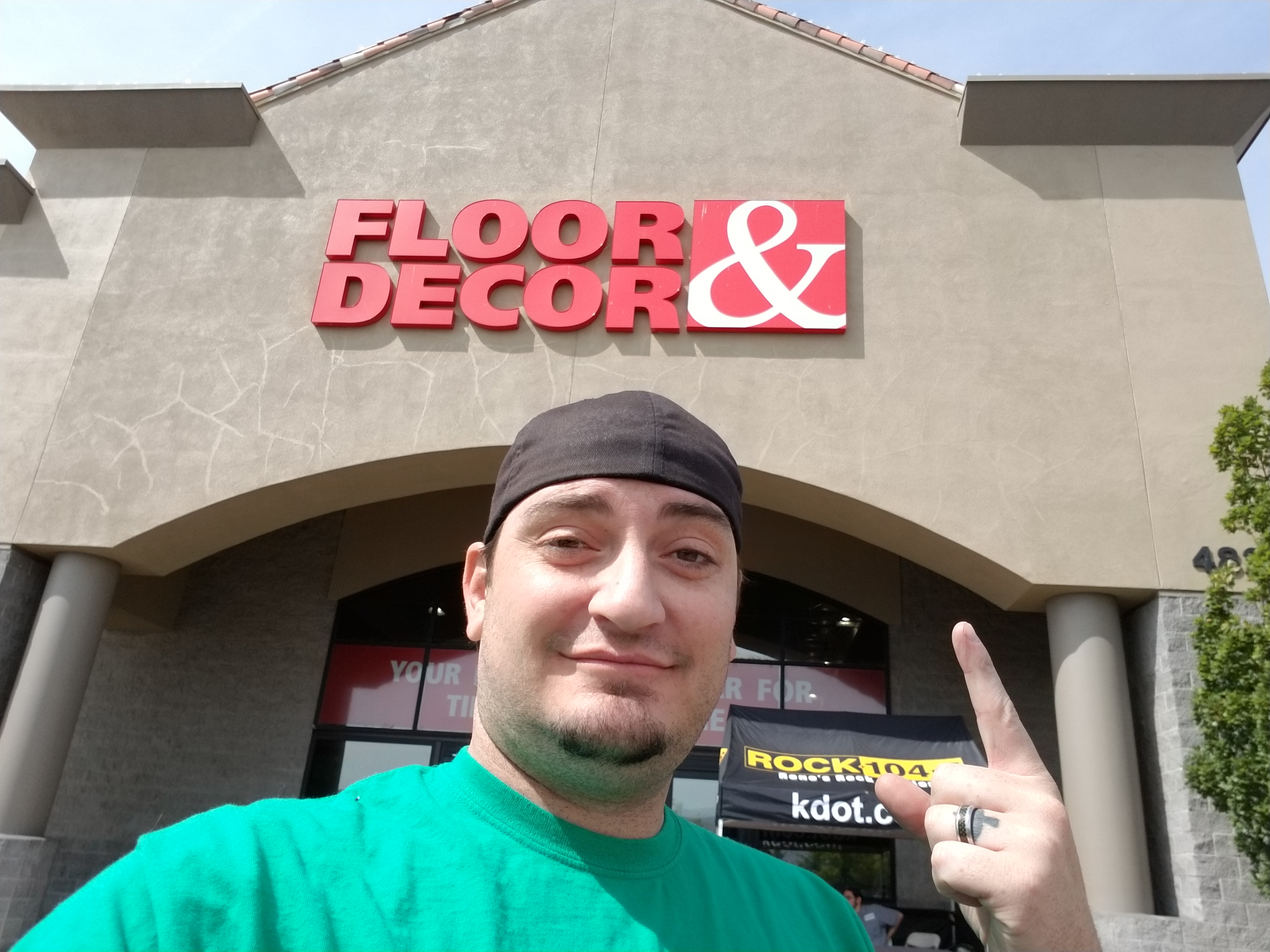 Kronik selfie pointing at a ROCK 104.5 KDOT tent outside Floor & Decor