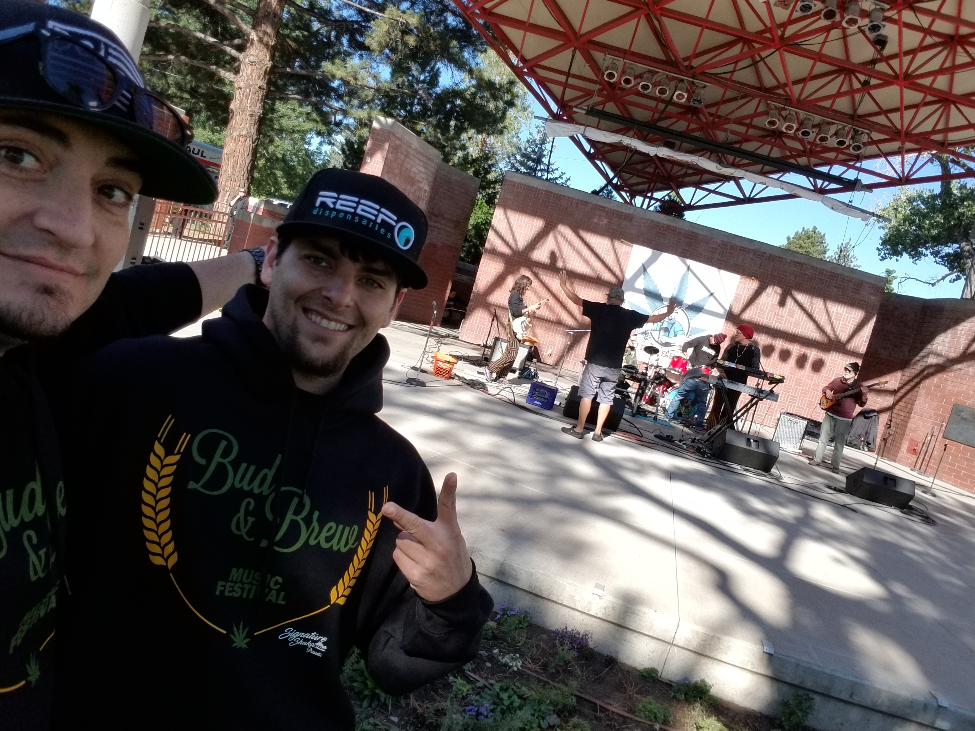 Kronik and a friend in Bud & Brew Music Festival hoodies with a live band on the outdoor stage