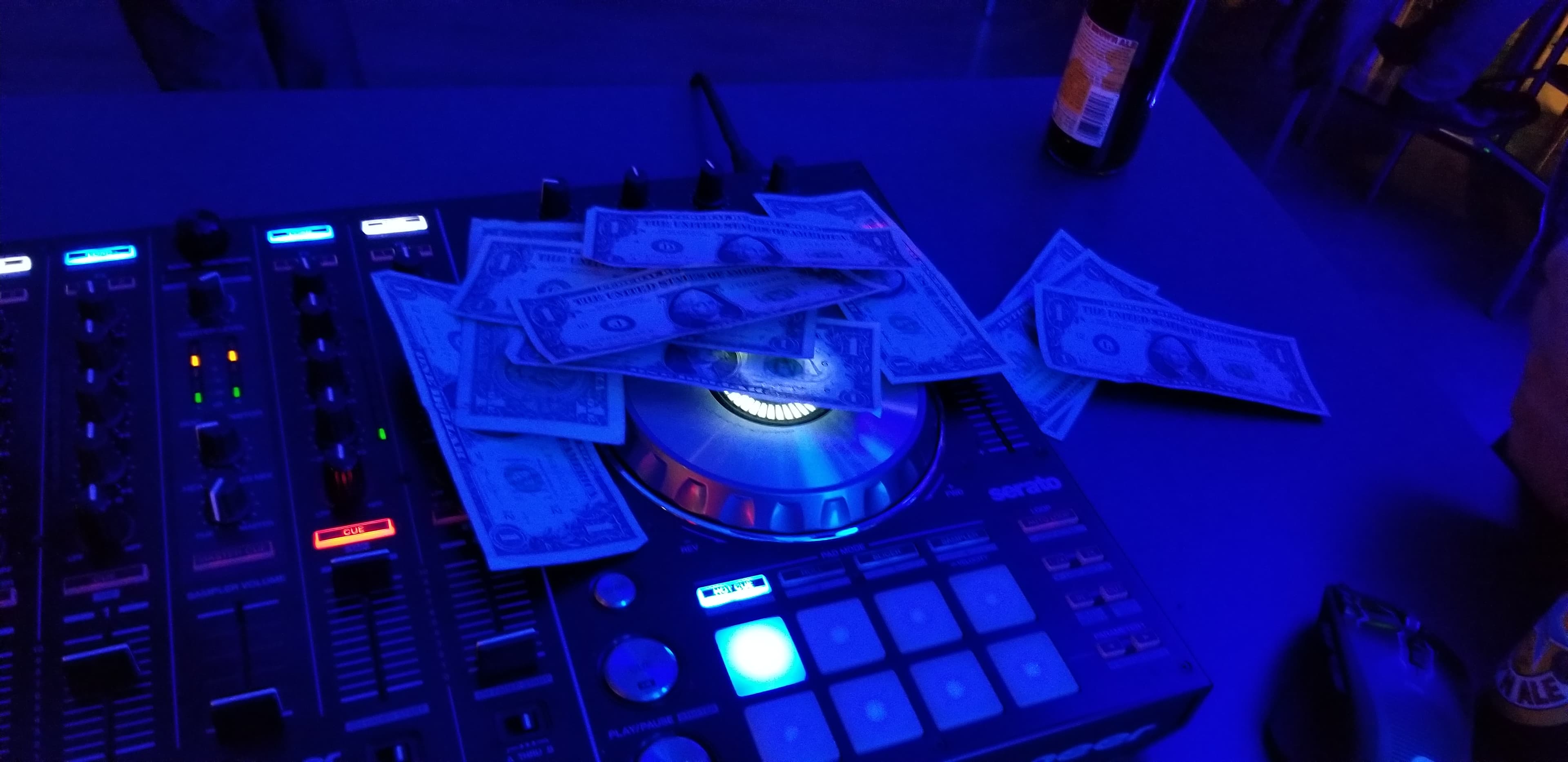 Serato DJ controller with cash tips on the jog wheel under blue club lighting