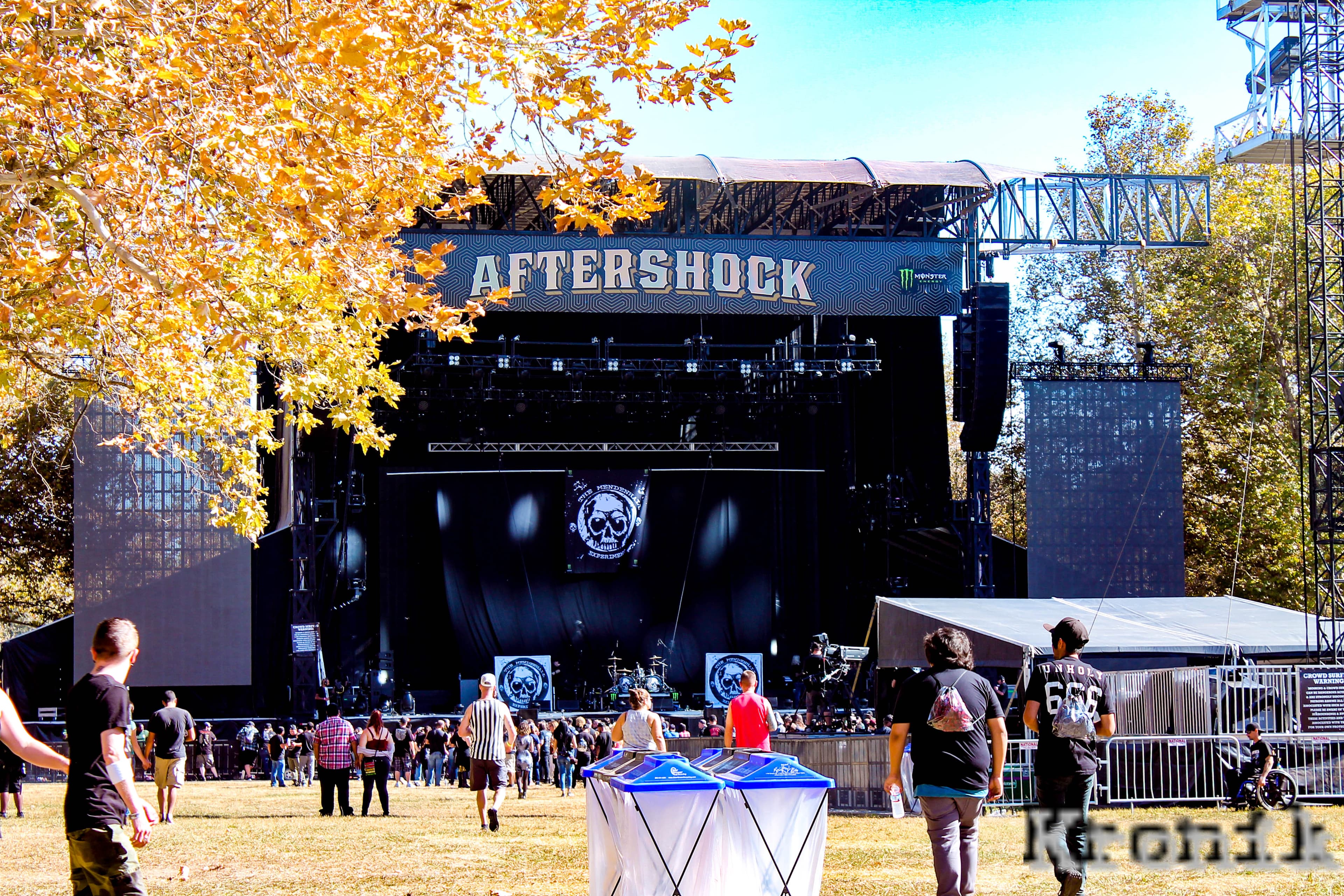 Crowd facing the Aftershock Festival main stage under autumn trees with Kronik watermark