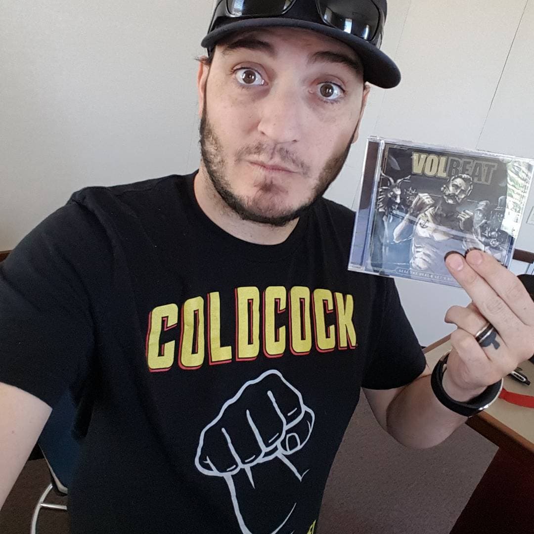 Kronik in Coldcock shirt holding a sealed Volbeat CD