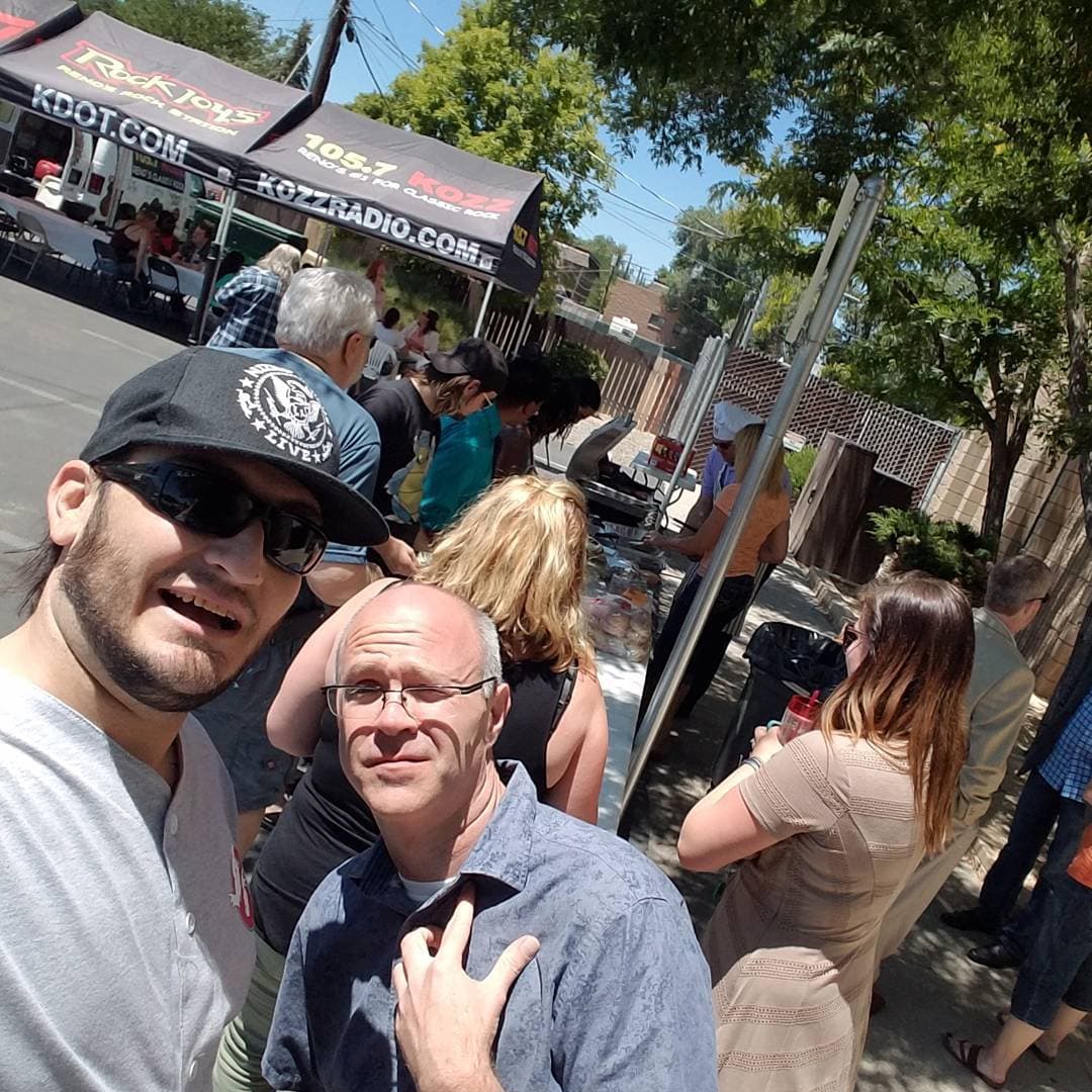 Kronik at an outdoor radio remote with Rock 104.5 KDOT and 105.7 KOZZ tents and a BBQ line